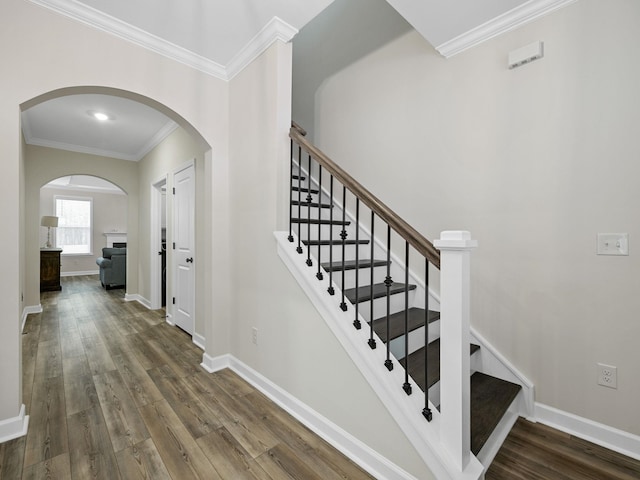 stairway featuring arched walkways, crown molding, wood finished floors, and baseboards