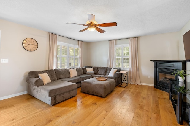 living room with a glass covered fireplace, a ceiling fan, healthy amount of natural light, and light wood finished floors