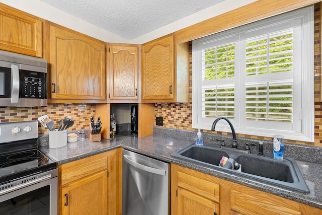 kitchen featuring stainless steel appliances, a sink, decorative backsplash, dark stone countertops, and a textured ceiling