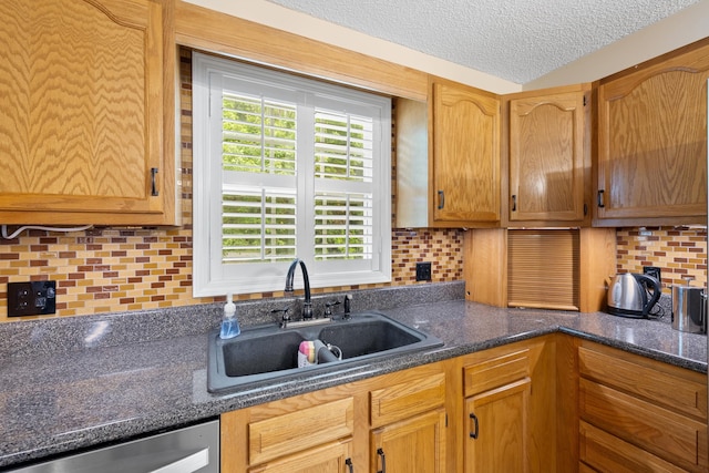 kitchen with a sink, stainless steel dishwasher, a textured ceiling, tasteful backsplash, and dark stone countertops