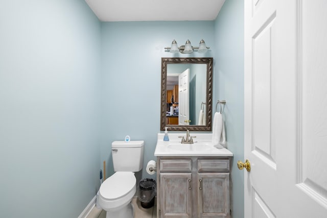 half bathroom featuring toilet, vanity, and baseboards