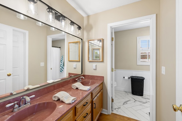 full bath with toilet, double vanity, and marble look tiles