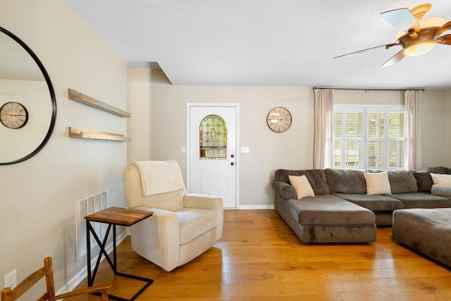 living room featuring light wood-style flooring, ceiling fan, baseboards, and a textured ceiling