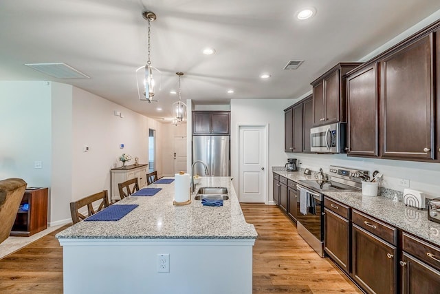 kitchen featuring stainless steel appliances, a sink, dark brown cabinets, light wood-style flooring, and recessed lighting