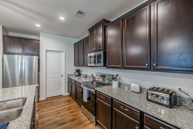 kitchen featuring stainless steel appliances, light wood-type flooring, dark brown cabinets, light stone counters, and recessed lighting