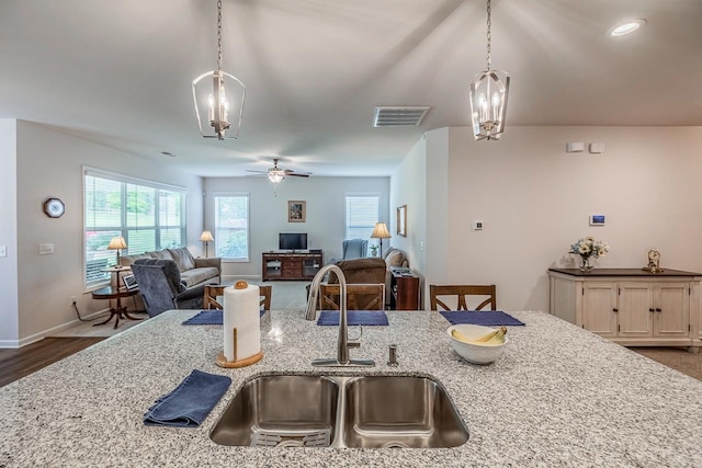 kitchen with a sink, light stone countertops, open floor plan, and decorative light fixtures