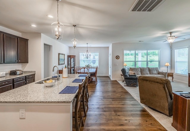 kitchen featuring a sink, dark brown cabinets, a breakfast bar area, light stone countertops, and healthy amount of natural light
