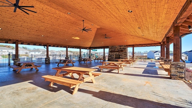 view of patio with ceiling fan, fence, an outdoor stone fireplace, and a gazebo