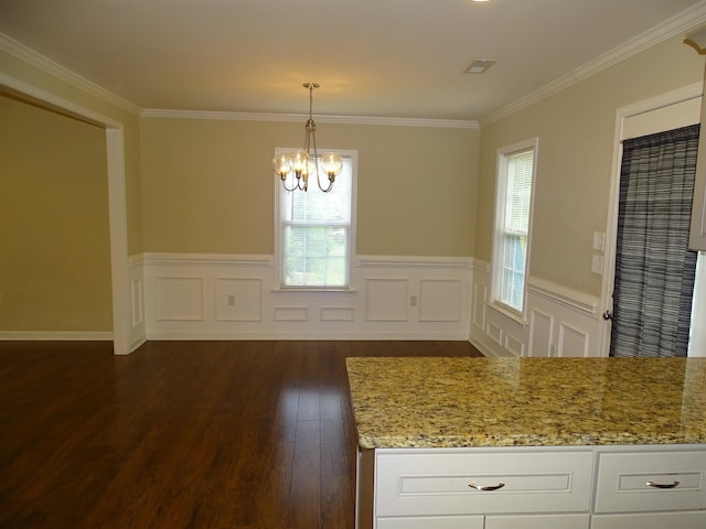 unfurnished dining area featuring crown molding, a chandelier, dark wood-style flooring, wainscoting, and a decorative wall