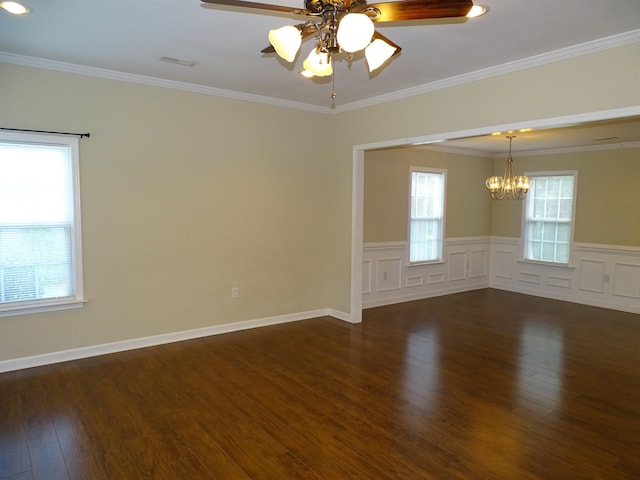 empty room with a chandelier, dark wood-style floors, healthy amount of natural light, ceiling fan, and a wainscoted wall