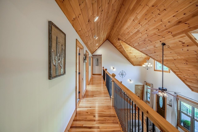 hallway featuring an upstairs landing, light wood-style flooring, wood ceiling, lofted ceiling, and a chandelier