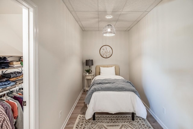 bedroom with wood finished floors, a paneled ceiling, and baseboards