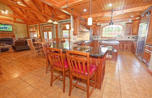 kitchen featuring wood ceiling, open floor plan, under cabinet range hood, brown cabinetry, and backsplash