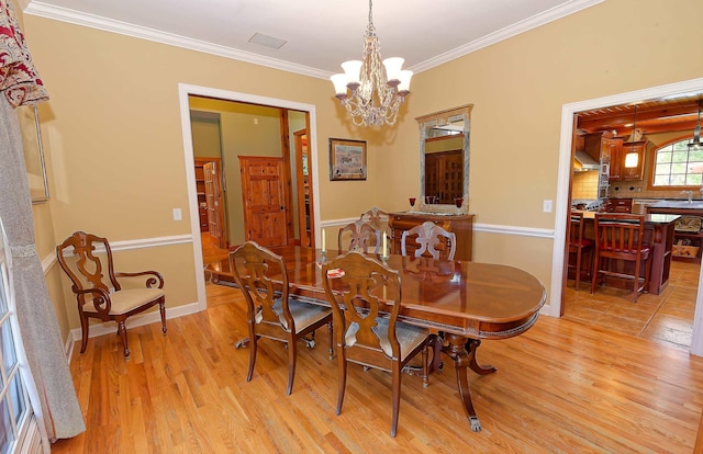 dining area featuring light wood-type flooring, a chandelier, crown molding, and baseboards