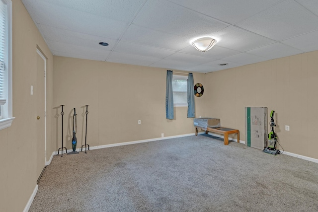 basement featuring a paneled ceiling, carpet floors, and baseboards