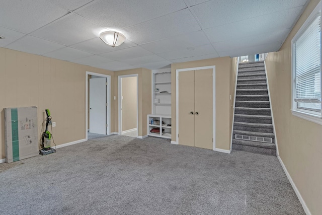 basement with carpet floors, a drop ceiling, stairs, and baseboards