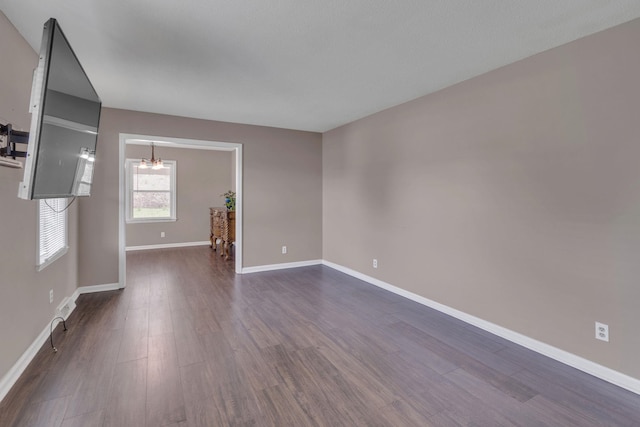 unfurnished room with dark wood finished floors, baseboards, and a chandelier