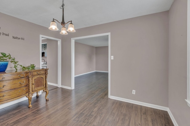 spare room with baseboards, a chandelier, and dark wood finished floors