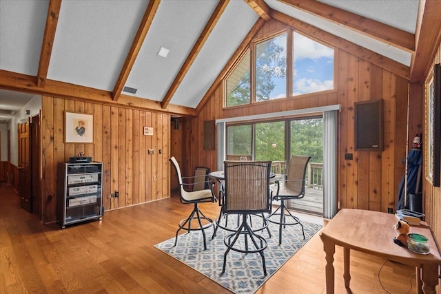 dining room with wooden walls, beamed ceiling, high vaulted ceiling, and wood finished floors