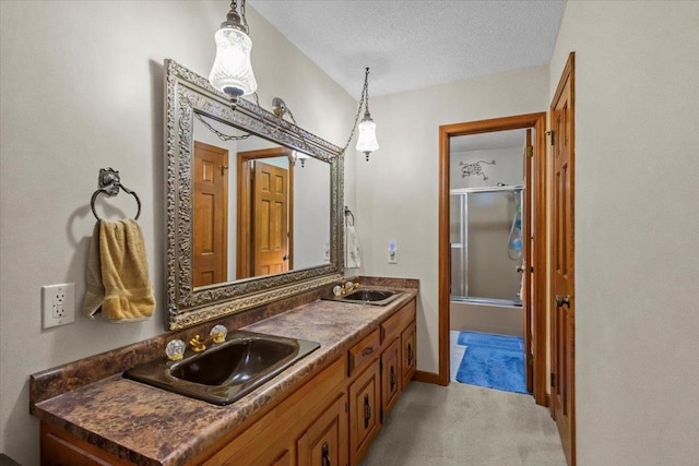 bathroom with double vanity, enclosed tub / shower combo, and a textured ceiling