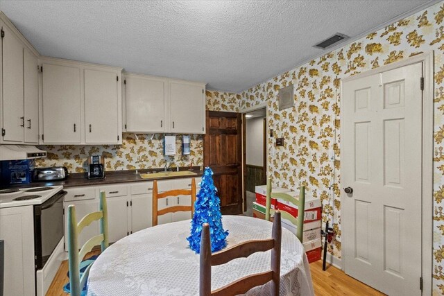 kitchen featuring wallpapered walls, light wood finished floors, electric range, a textured ceiling, and a sink