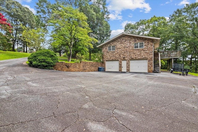 view of property exterior with stairs, a garage, asphalt driveway, a deck, and brick siding