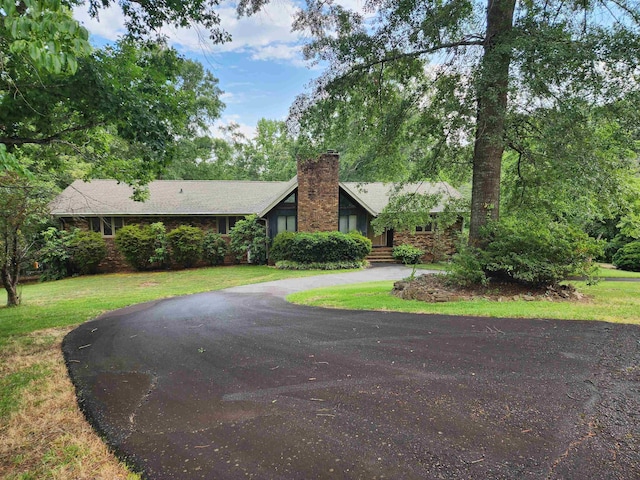 view of front of property with curved driveway, a chimney, and a front lawn