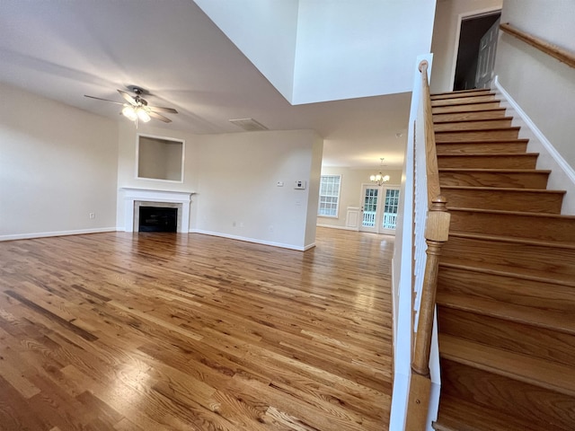 unfurnished living room with ceiling fan, wood finished floors, a fireplace, stairway, and a chandelier