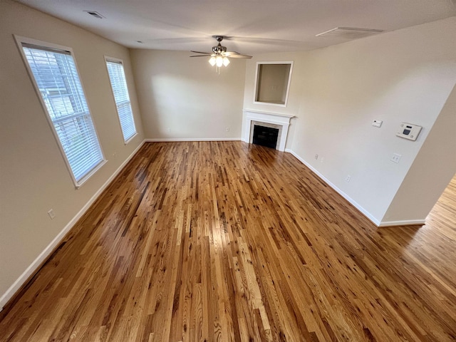 unfurnished living room with wood finished floors, a ceiling fan, baseboards, and a fireplace