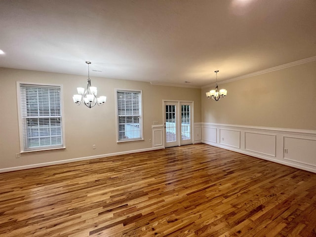 empty room featuring a chandelier, wood finished floors, crown molding, and a wainscoted wall