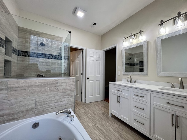 bathroom with tiled shower, a tub with jets, double vanity, and wood finished floors