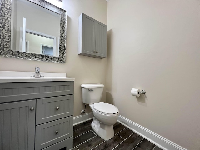 half bath with baseboards, toilet, wood tiled floors, and vanity