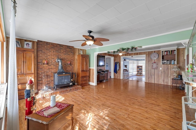 109 Pinewood, Clinton, SC 29325 - living room featuring a wood stove, ceiling fan, wood walls, light wood-style flooring, and crown molding