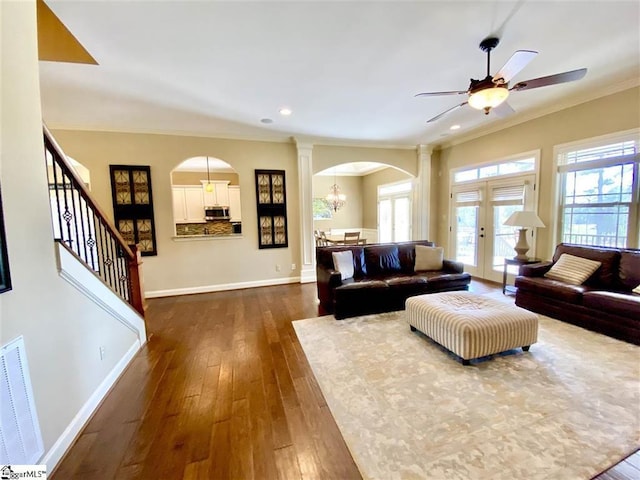 living room with dark wood-type flooring, ornate columns, crown molding, and ceiling fan with notable chandelier