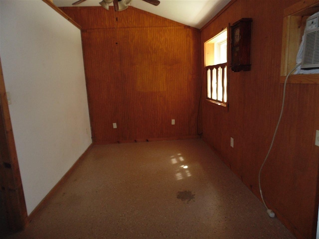 empty room featuring ceiling fan, wooden walls, and vaulted ceiling