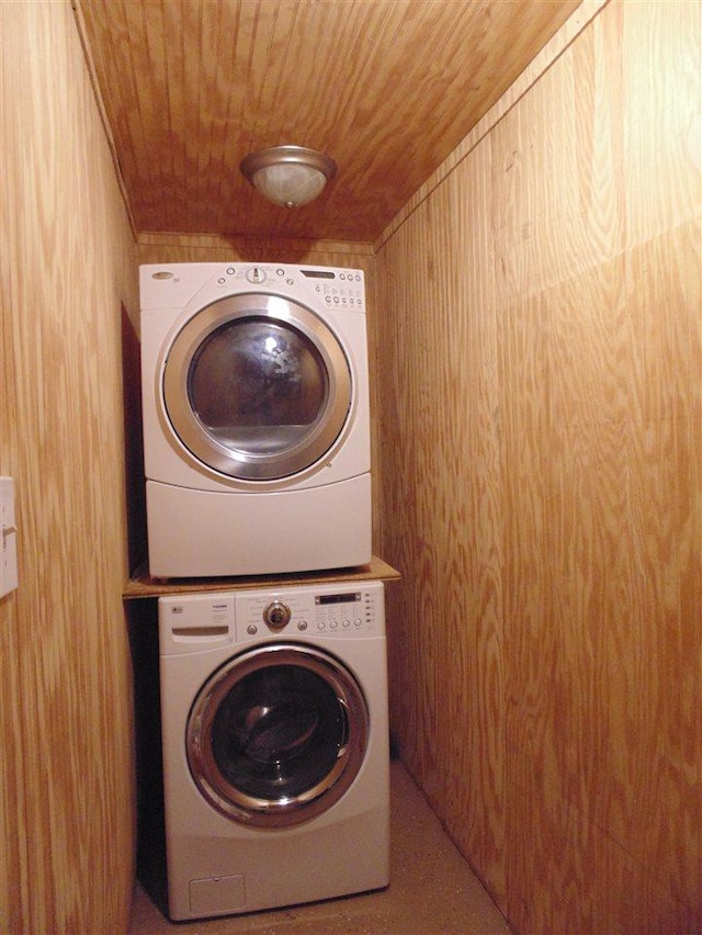 clothes washing area featuring wood ceiling, stacked washer and clothes dryer, and wooden walls