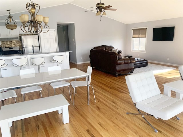 dining area featuring light hardwood / wood-style floors, ceiling fan with notable chandelier, and vaulted ceiling