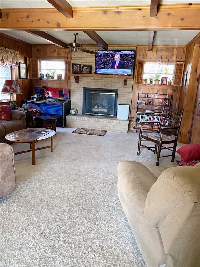 carpeted living room with ceiling fan, wooden walls, beamed ceiling, and a brick fireplace