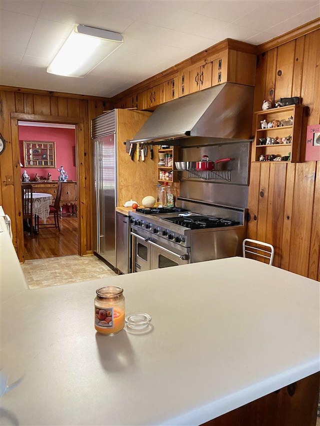 kitchen featuring range hood, wooden walls, high end appliances, and light hardwood / wood-style flooring