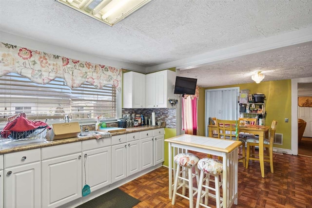 kitchen with backsplash, a textured ceiling, dark parquet flooring, and white cabinetry