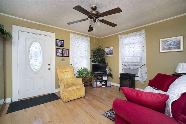 living room with ceiling fan, ornamental molding, light hardwood / wood-style floors, and a textured ceiling