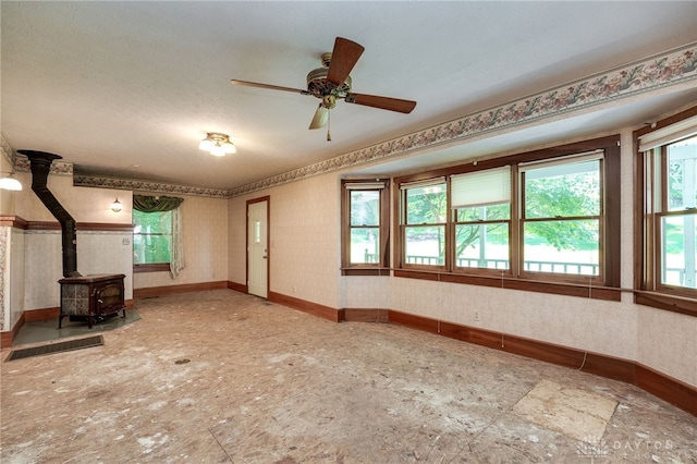 unfurnished living room featuring a textured ceiling, ceiling fan, a wealth of natural light, and a wood stove