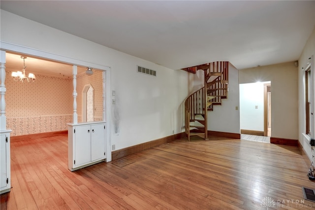 unfurnished living room featuring a chandelier and light wood-type flooring