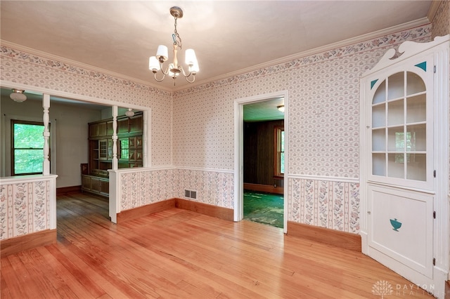 empty room with an inviting chandelier, hardwood / wood-style flooring, and crown molding