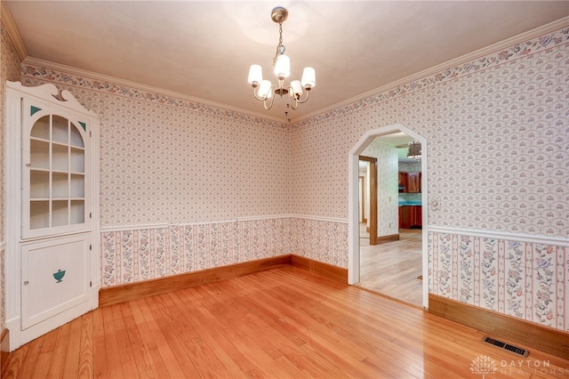 spare room featuring a notable chandelier, light hardwood / wood-style flooring, and ornamental molding