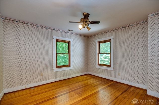 spare room featuring ceiling fan, wood-type flooring, and a healthy amount of sunlight