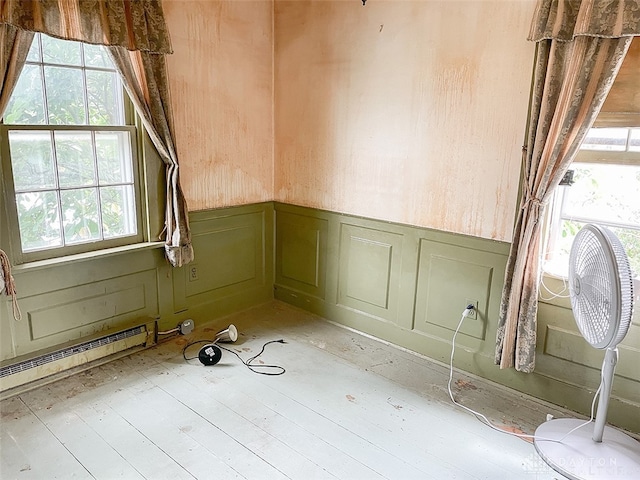 spare room featuring a baseboard heating unit, hardwood / wood-style flooring, and wooden walls