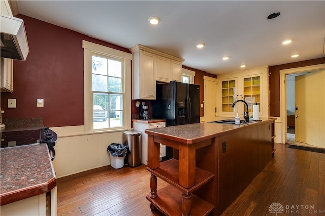 kitchen with black refrigerator with ice dispenser, dark hardwood / wood-style flooring, stove, range hood, and sink