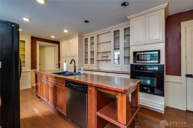 kitchen featuring black appliances, sink, a center island with sink, and hardwood / wood-style floors