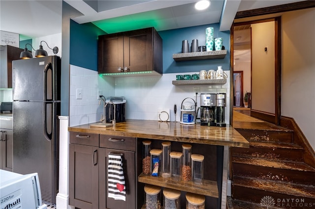 kitchen featuring decorative backsplash, butcher block countertops, dark brown cabinets, and black fridge